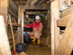 Zwei Personen mit Helm hocken im Stollen und lächeln in die Kamera.