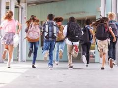 Kinder mit Schulranzen laufen auf einen Eingang zu