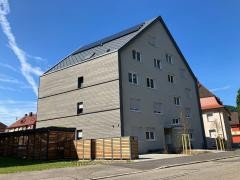 Vor blauem Himmel steht ein graues Mehrfamilienhaus.