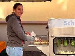 Eine Frau steht an einer Spargel-Schäl-Maschine. Sie lächelt.