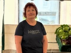 Eine Frau steht hinter einem Marktstand. Auf dem Bild ist auch Salat zu erkennen.