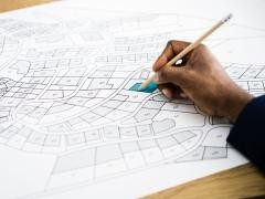 Ein Hand liegt auf einem Plan. Eine Fläche ist blau eingezeichnet.