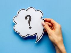 Eine Hand hält ein Fragezeichen vor einem blauen Hintergrund.