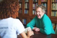 Zwei Menschen - eine jüngere und eine ältere Person - sitzen an einem Tisch und lachen.