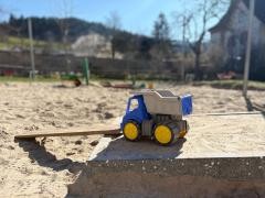 Ein Spielzeugbagger steht in einem Sandkasten.