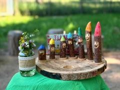 Verschiedene Figürchen stehen auf einem Brett draußen. Daneben steht ein Glas mit selbst geplfückten Blumen.