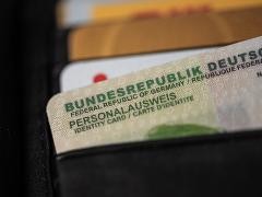 Ein deutscher Personalausweis steckt in einem Fach einer schwarzen Brieftasche. Nur ein Teil des Ausweises ist sichtbar, mit der Aufschrift „BUNDESREPUBLIK DEUTSCHLAND“ und „PERSONALAUSWEIS“. Weitere Kartenfächer mit verschiedenen Karten befinden sich darüber.