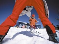 Ein Kind auf Ski fährt auf eine Erwachsene zu.
