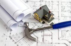 Auf einem Bauplan steht ein Modellhaus. Daneben liegt ein Hammer.