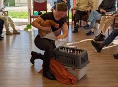 Eine Frau hält ein Huhn in einer Tagespflege in der Hand. Rund um die Frau sitzen mehrere Leute. Von ihnen sind nur die Beine zu sehen.