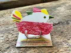 Auf einem Holztisch steht ein gebastelter Vogel aus Papier.