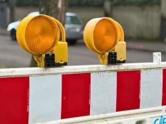 An einem rot-weiß gestreiften Absperrzaun hängen zwei orangene Leuchten.