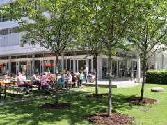 Das Gisela-Sick-Bildungshaus von außen. Im Garten sind Bierbänke aufgestellt. An den Bierbänken sitzen viele Leute.