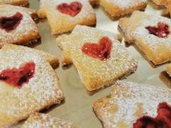 Auf einem Backblech liegen Keks in Form eines Hauses. Jeder Keks hat ein rotes Marmeladen-Herz.