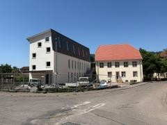 Bild einer Baustelle: An ein altes Gebäude schließt sich ein Nebau an. Das Gebäude ist mit einem Zaun abgesperrt.