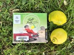 Auf einer Wiese liegt das Hörbuch "Tante Poldi und der schöne Antonio". Daneben liegen zwei Zitronen.
