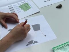 Eine Person durchläuft einen Demenzparcours. Auf einem Plan muss sie mit einem Stift einen Weg einzeichnen.