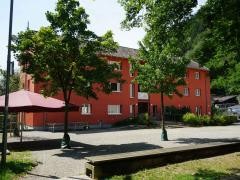Das Rote Haus von außen: vor dem roten Gebäude stehen mehrere Bäume. Die Sonne scheint.
