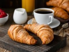 Auf einem Tisch ist ein Frühstück gerichtet. Croissants und ein Kaffee stehen dort.