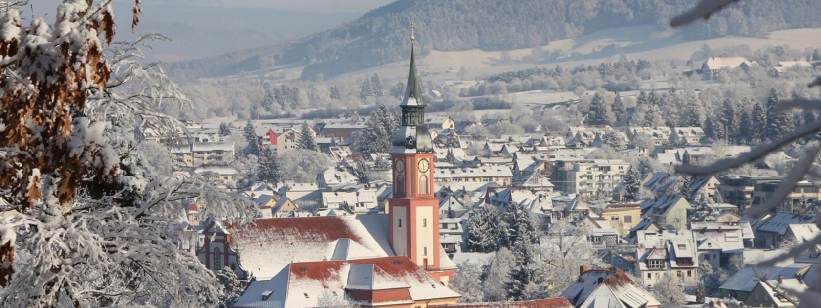 Verschneite St-Margarethen Kirche. Im Hintergrund ist Waldkirch zu erkennen. Auf den Dächern liegt Schnee.